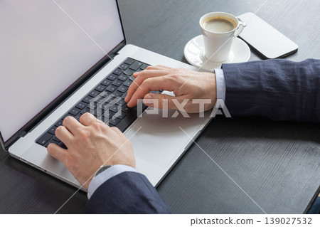 Close up of hands typing on laptop keyboard with coffee cup on desk in modern workspace Close up of hands typing on laptop keyboard with coffee cup on desk in modern workspace 139027532