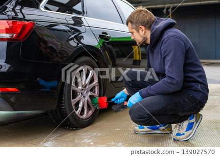 Man cleaning car wheel with brush at washing station automotive maintenance 139027570