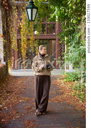 Woman walking in autumn park surrounded by trees and falling leaves Woman walking in autumn park surrounded by trees and falling leaves 139027599