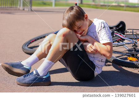 Boy sitting on ground after bicycle fall holding injured knee outdoors Boy sitting on ground after bicycle fall holding injured knee outdoors 139027601