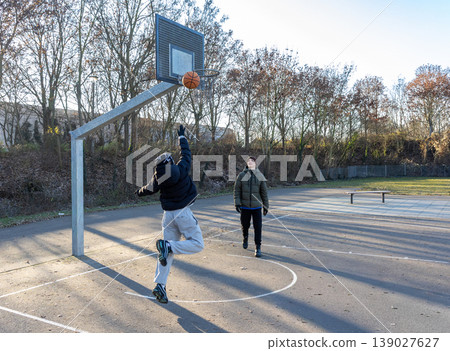 Teen boy making basketball layup shot outdoor court sport action training lifestyle Teen boy making basketball layup shot outdoor court sport action training lifestyle 139027627