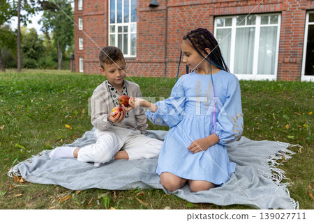 Boy and girl sitting on a picnic blanket sharing fresh apples. Boy and girl sitting on a picnic blanket sharing fresh apples. 139027711