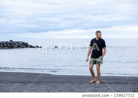 Man Walking on Black Sand Beach Near Ocean Calm Travel Freedom Lifestyle Concept 139027722