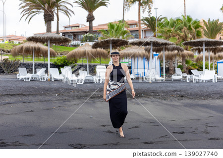 Confident Woman Walking on Black Sand Beach with Palm Trees Tropical Resort Lifestyle Confident Woman Walking on Black Sand Beach with Palm Trees Tropical Resort Lifestyle 139027740