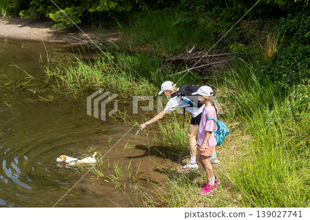 Woman And Young Girl Walking Small Dog Near River In Green Summer Landscape 139027741