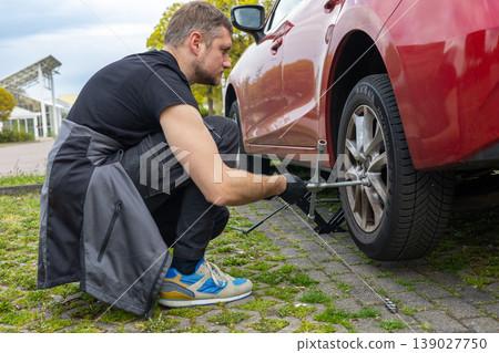 Man changing car tire with jack and wrench on roadside pavement in daylight 139027750