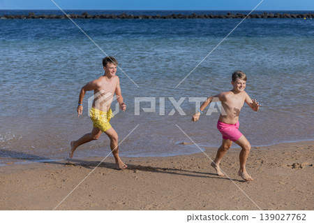 Smiling Brothers Running On Beach Sand With Blue Sea Background In Bright Summer Smiling Brothers Running On Beach Sand With Blue Sea Background In Bright Summer 139027762