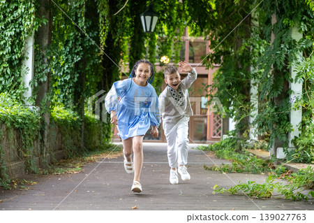 Energetic boy and girl running through a lush green walkway. Energetic boy and girl running through a lush green walkway. 139027763