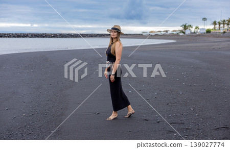 Woman in Black Dress Walking on Volcanic Beach Under Stormy Sky 139027774