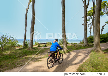 Woman riding bicycles along a sandy forest path near the sea. Woman riding bicycles along a sandy forest path near the sea. 139027831