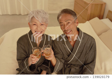 Senior couple drinking whiskey in the bedroom, portrait, looking at camera Senior couple drinking whiskey in the bedroom, portrait, looking at camera 139028179