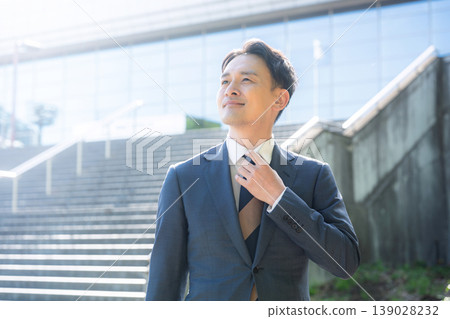 A refreshing, suit-wearing salesman, with a building in the background, looks towards the future—a business image symbolizing career success and growth. A refreshing, suit-wearing salesman, with a building in the background, looks towards the future—a business image symbolizing career success and growth. 139028232
