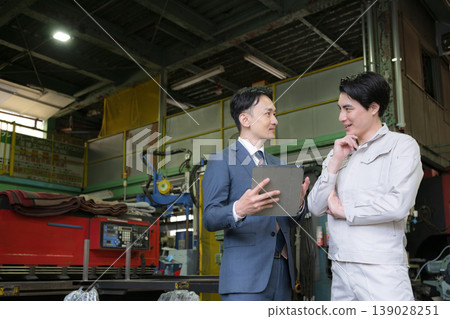 Two people: a factory worker holding a tablet in a manufacturing plant, and a salesman having a meeting with a credit union or other businesspeople. Two people: a factory worker holding a tablet in a manufacturing plant, and a salesman having a meeting with a credit union or other businesspeople. 139028251