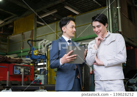 兩個人:一個是工廠工人,在製造廠裡拿著平板電腦;另一個是銷售員,正在與信用社或其他商人開會。 兩個人:一個是工廠工人,在製造廠裡拿著平板電腦;另一個是銷售員,正在與信用社或其他商人開會。 139028252