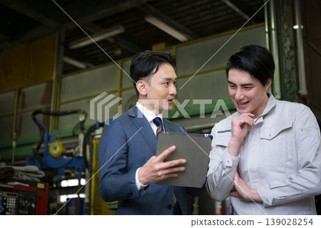 兩個人:一個是工廠工人,在製造廠裡拿著平板電腦;另一個是銷售員,正在與信用社或其他商人開會。 兩個人:一個是工廠工人,在製造廠裡拿著平板電腦;另一個是銷售員,正在與信用社或其他商人開會。 139028254