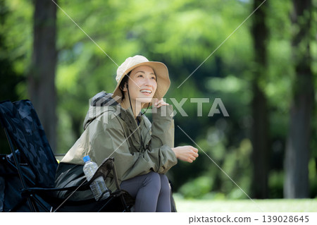 一位微笑的女子獨自坐在鬱鬱蔥蔥的森林中的露營椅上，欣賞著周圍的景色。 139028645