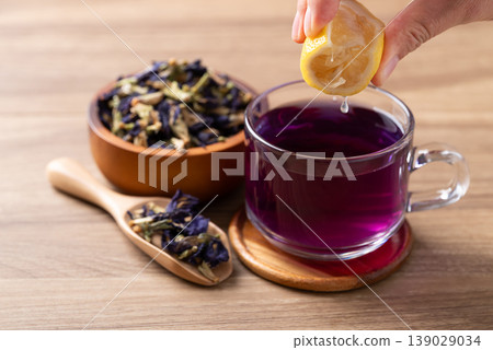 Hand squeezing lemon into a glass of blue butterfly pea tea to change color to purple Hand squeezing lemon into a glass of blue butterfly pea tea to change color to purple 139029034