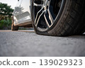 Close-up of a flat car tire on a white vehicle parked on a gravel road 139029323