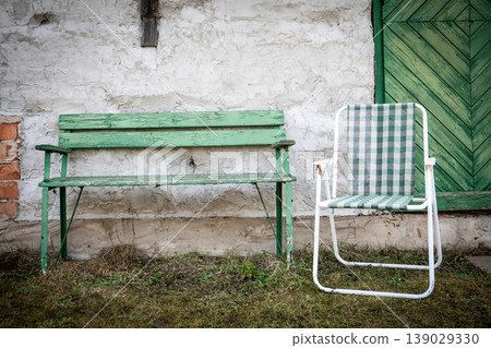 Green Wooden Bench and Checkered Chair Against Rustic Wall Green Wooden Bench and Checkered Chair Against Rustic Wall 139029330