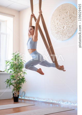 Body balance. Hammock yoga. Young woman doing fitness muscle session hanging in light studio air holding fabric equipment support. 139029405