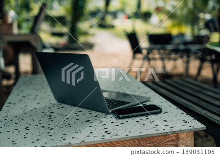 Laptop computer and smartphone placed on a table in a relaxed outdoor tropical cafe setting. Laptop computer and smartphone placed on a table in a relaxed outdoor tropical cafe setting. 139031105
