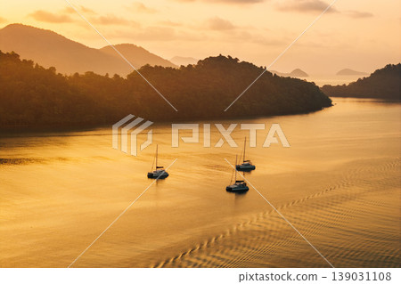 Aerial golden hour landscape of sailing catamarans anchored in a serene tropical bay surrounded by island silhouettes. Aerial golden hour landscape of sailing catamarans anchored in a serene tropical bay surrounded by island silhouettes. 139031108