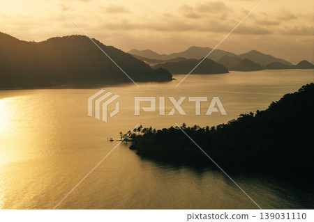 Atmospheric aerial landscape of overlapping tropical island silhouettes in the ocean at misty sunrise. 139031110
