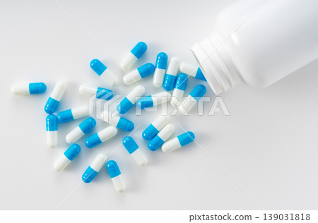 藍白相間的膠囊從白色瓶子中傾瀉而出；俯視圖，白色背景。 139031818