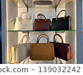 Yogyakarta, Indonesia - March 18th 2026: Six elegant women's handbags in various colors are meticulously displayed on clear glass shelves within a brightly lit retail store 139032242