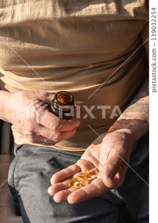 Mans hands holding a handful of fish oil capsules poured from a brown bottle, promoting daily health and wellness. Healthy lifestyle, self-care Mans hands holding a handful of fish oil capsules poured from a brown bottle, promoting daily health and wellness. Healthy lifestyle, self-care 139032254