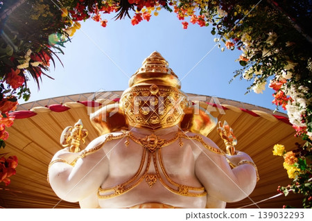 Back View of Large Golden and White Ganesha Statue Framed by Flowers under Clear Blue Sky 139032293