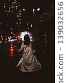 The back view of a person holding an umbrella in the city late at night, on a rainy street corner. 139032656