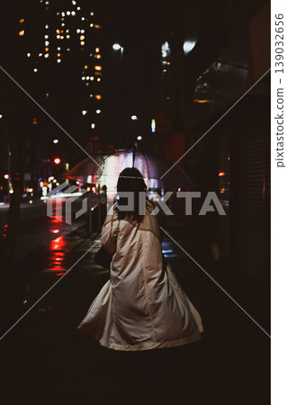 The back view of a person holding an umbrella in the city late at night, on a rainy street corner. The back view of a person holding an umbrella in the city late at night, on a rainy street corner. 139032656