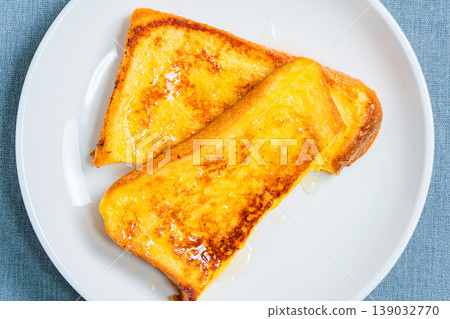 A close-up of honey-covered French toast, presented on a white plate, resembling a breakfast image. 139032770