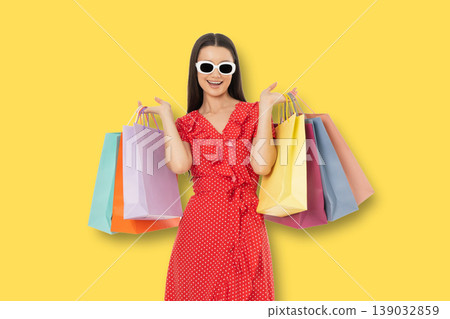 Woman poses with colorful shopping bags on yellow background Woman poses with colorful shopping bags on yellow background 139032859