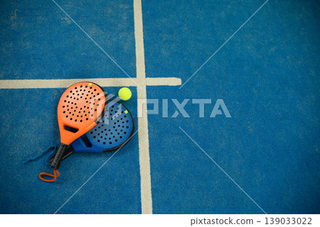 Padel rackets rest on blue court with a ball nearby Padel rackets rest on blue court with a ball nearby 139033022