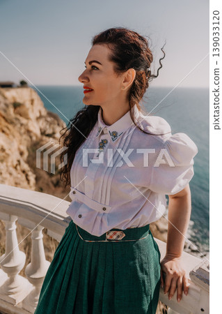 Woman coast fashion enjoying scenic ocean view from a balcony in vintage white blouse and green skirt during sunny summer holiday 139033120