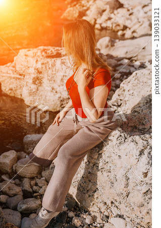 Woman sitting coast relaxing on rocky shoreline during golden sunset light outdoors at sea 139033121