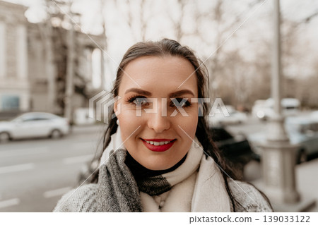 Woman portrait smiling young brunette female wearing knit sweater and scarf on blurred city street during autumn Woman portrait smiling young brunette female wearing knit sweater and scarf on blurred city street during autumn 139033122