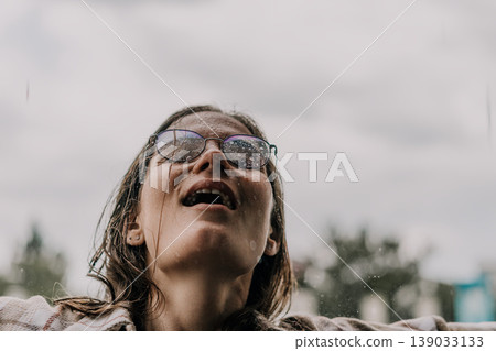 Woman rain glasses looking up at the sky with a wet face during a summer storm feeling refreshed and free Woman rain glasses looking up at the sky with a wet face during a summer storm feeling refreshed and free 139033133