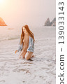 Woman beach ocean kneeling in sea waves at sunset with rocky cliffs providing a serene and peaceful summer vibe 139033143