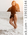 Swimsuit beach model posing in black swimwear among ocean waves and coastal rock formation during sunset golden hour 139033144