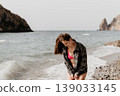 Woman beach ocean Brunette woman in pink bikini and flannel shirt stands on a rocky shore with waves and cliffs 139033145