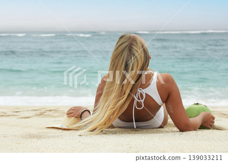 Woman enjoys the beach while holding a coconut Woman enjoys the beach while holding a coconut 139033211