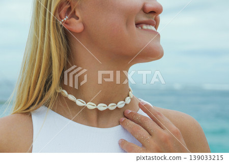 Woman smiles while wearing seashell necklace by the sea 139033215