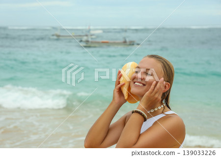 Woman smiles while holding seashell by the water Woman smiles while holding seashell by the water 139033226