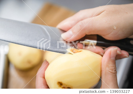 A woman peels potatoes with a knife. A woman peels potatoes with a knife. 139033227