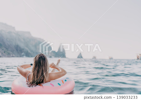 Woman, ocean, relaxing. Woman floats on pink donut ring in the sea enjoying summer vacation with copy space. Woman, ocean, relaxing. Woman floats on pink donut ring in the sea enjoying summer vacation with copy space. 139033233