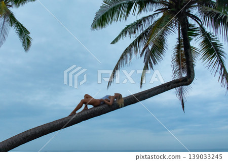 Woman lying on a palm tree branch near the ocean Woman lying on a palm tree branch near the ocean 139033245