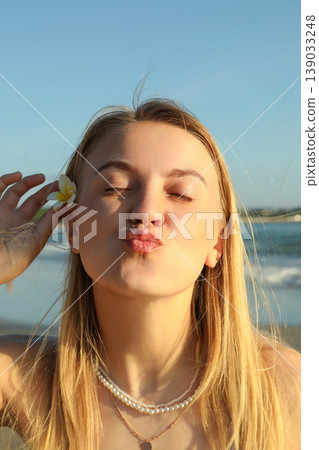 Woman smiles and poses with a flower near the beach 139033248